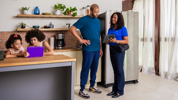 an energy advisor speaking to a father in his kitchen while his daughters watch something on their tablet