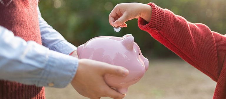 a child putting  a coin in a piggy bank