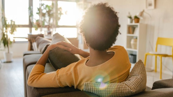 rear view of a woman sitting on a couch in her brightly lit modern living room 