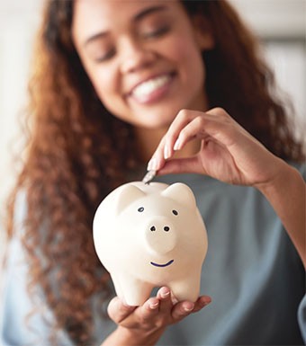 a woman smiling and dropping a coin in a piggy bank